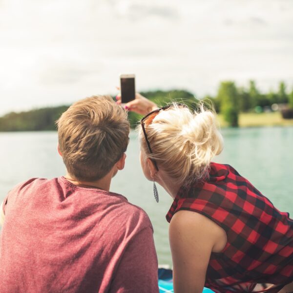 woman and woman sitting on dock both holding one smartphone