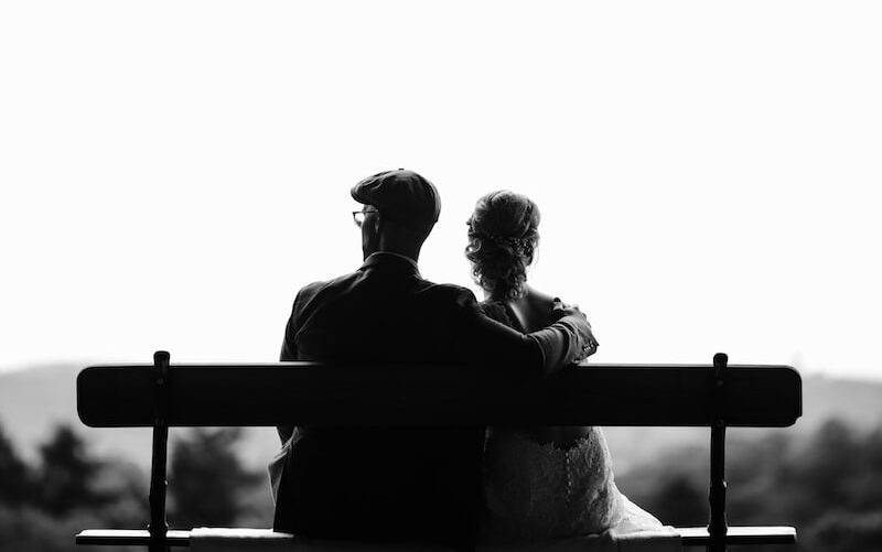 couple sitting on bench under tree grayscale photography